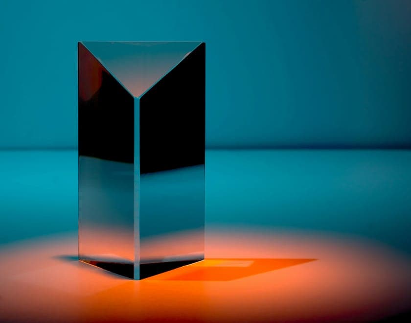 Glass prism award standing in a pool of orange light on a teal backdrop.