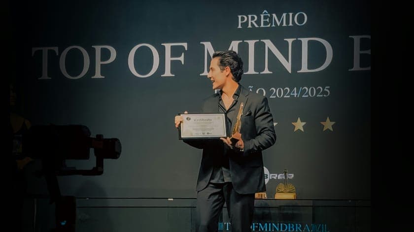 Man in a dark suit holding a certificate and a trophy on an awards stage.