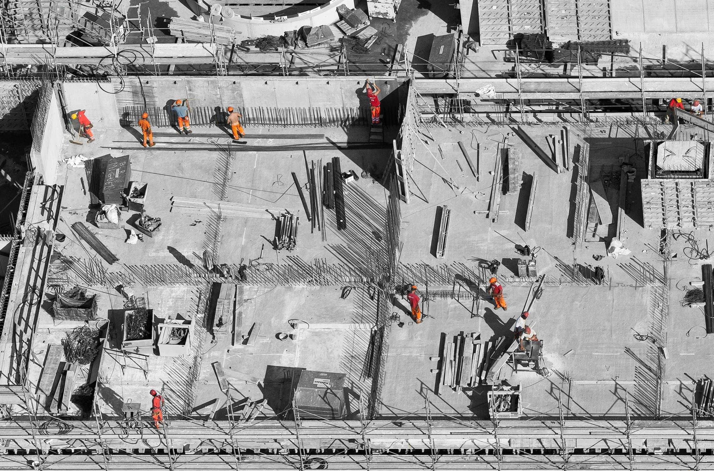 Aerial view of workers in orange suits on a concrete deck laid with steel rebar.