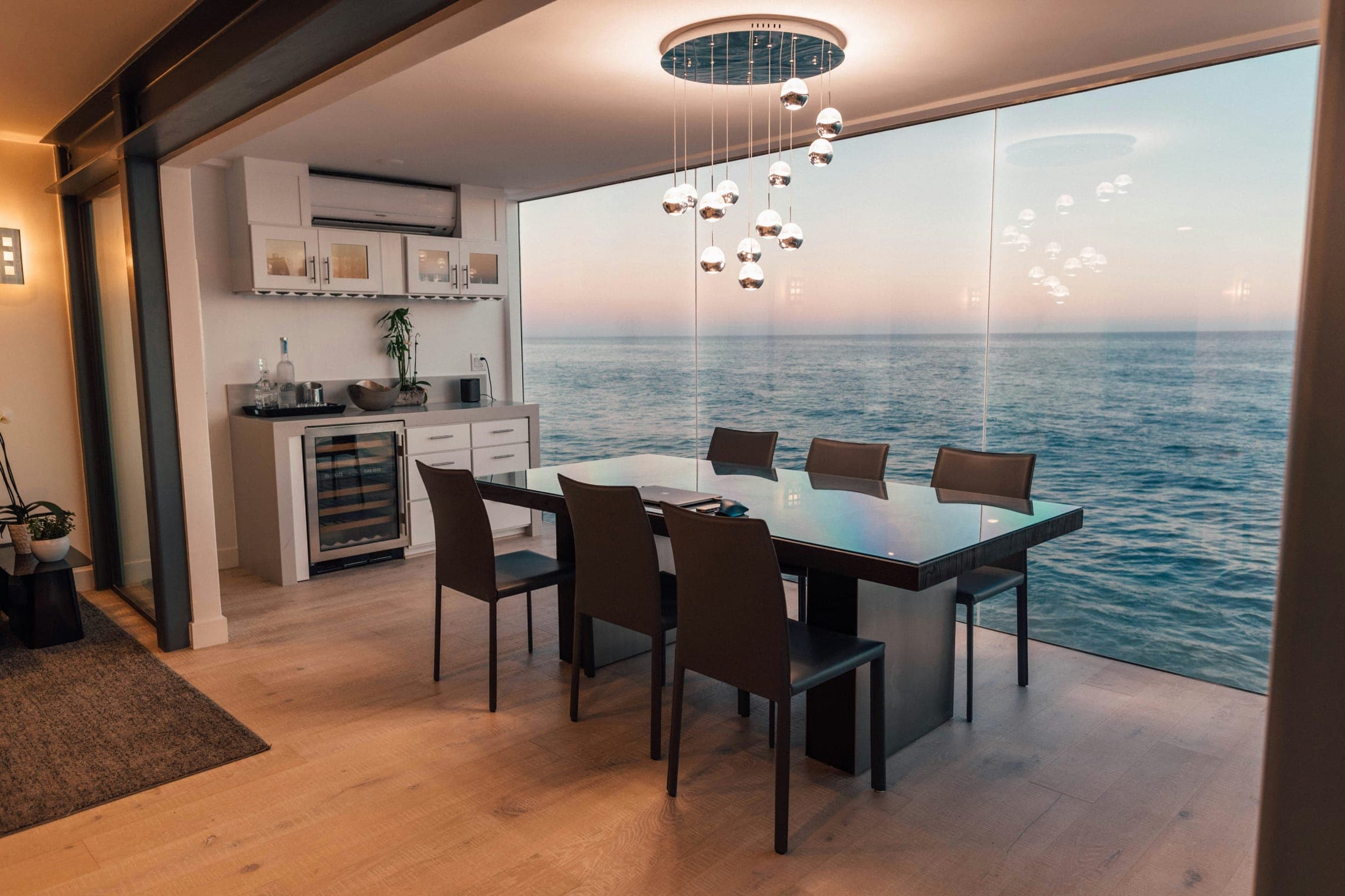 Dining room with dark table, leather chairs and a glass wall overlooking the sea at dusk.
