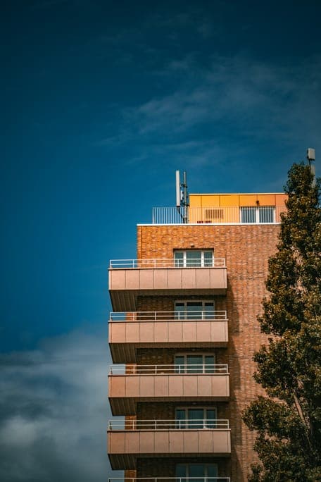 Brick building with stacked balconies and an orange rooftop level against a deep blue sky.