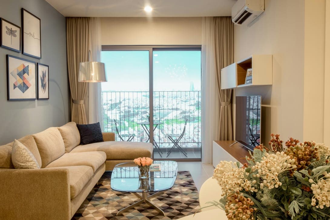 Living room with beige sectional sofa, glass coffee table and balcony overlooking a city.