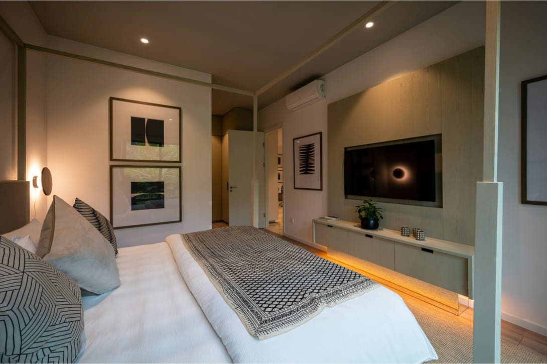 Softly lit bedroom with white bedding, patterned throw, framed prints and wall-mounted television.
