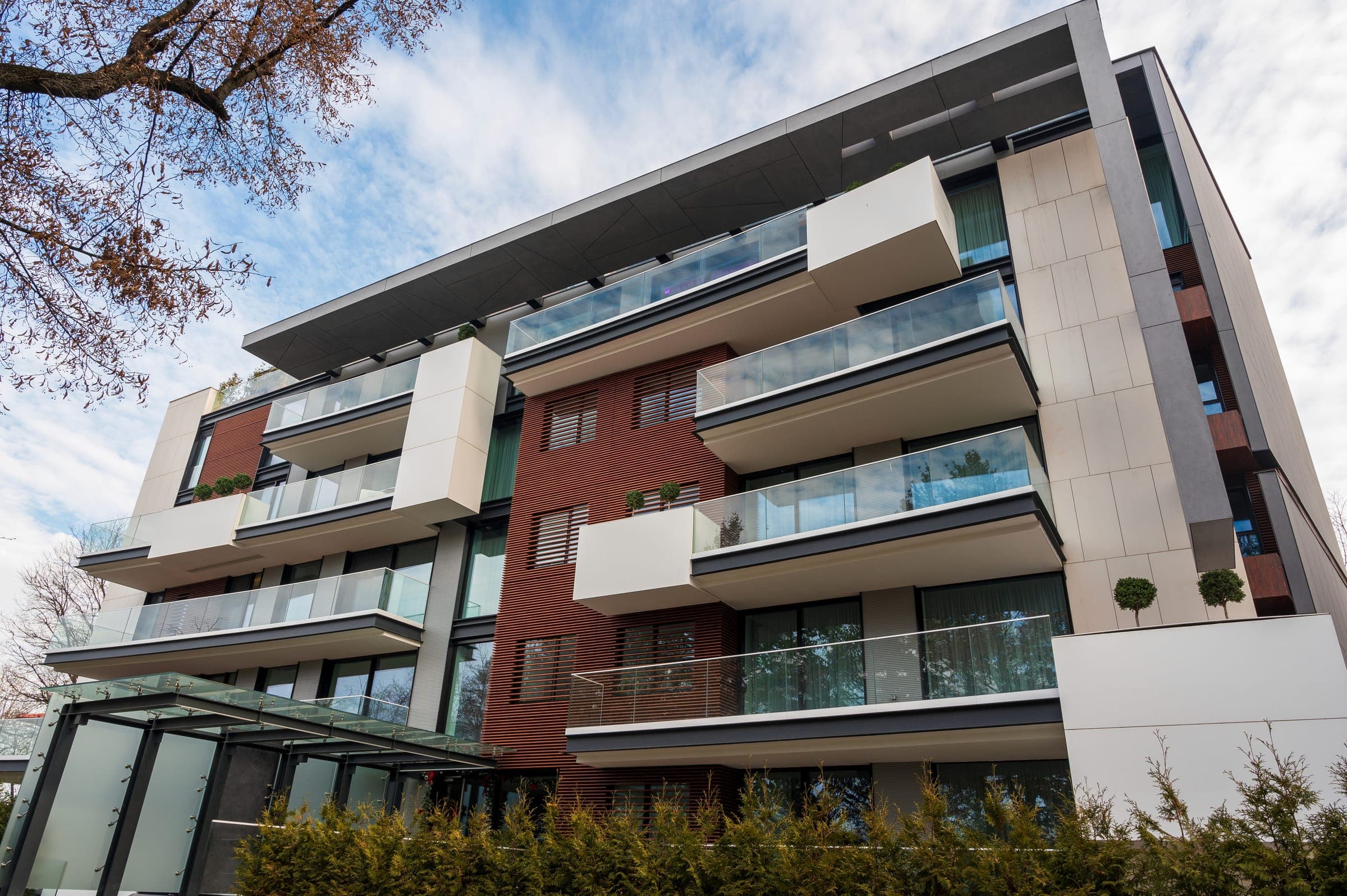 Low-angle view of a modern residence with white and brick facades and glass balconies.