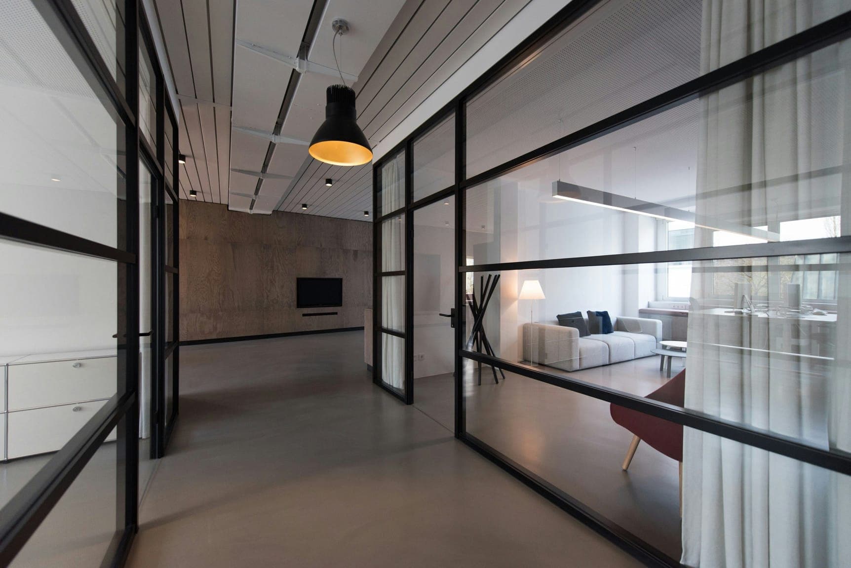 Black-framed glass partitions opening onto a lounge with grey sofa and pendant lamp.