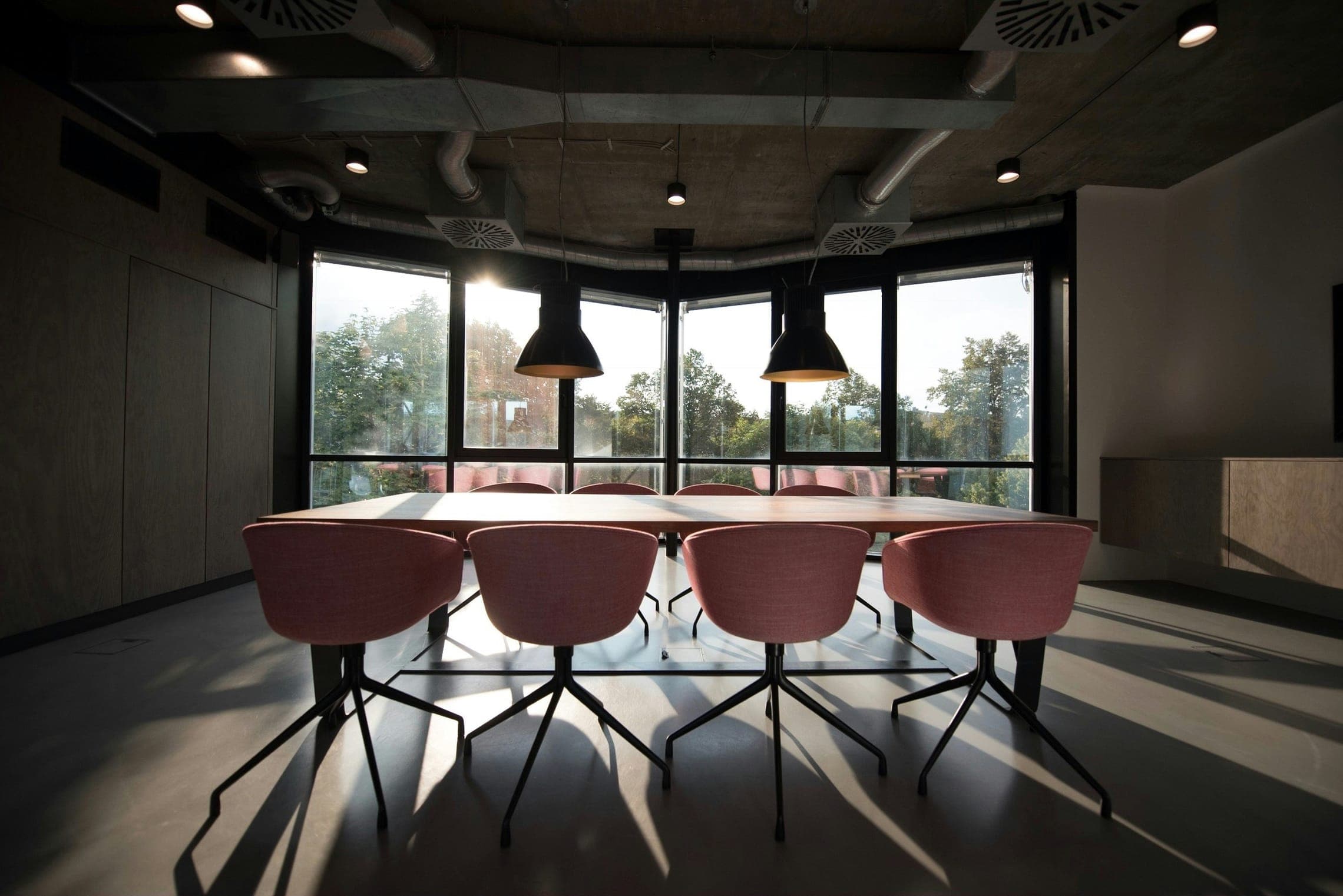 Backlit boardroom with pink chairs around a long table before a curved wall of windows.