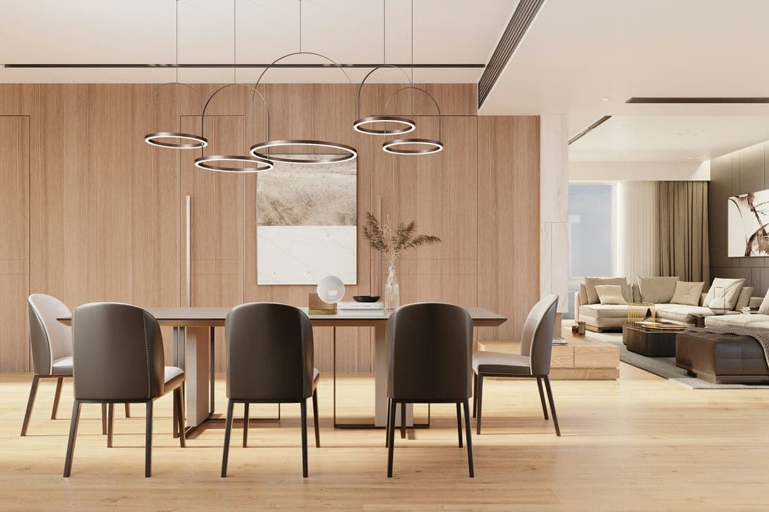 Dining area with wood-panelled wall, grey chairs, ring chandeliers and an open living room.