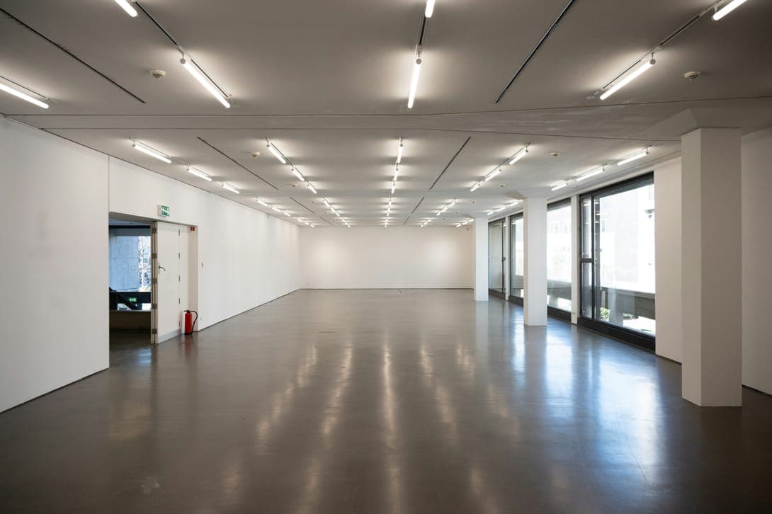 Long empty white hall with glossy floor, strip lights, columns and glazed side wall.