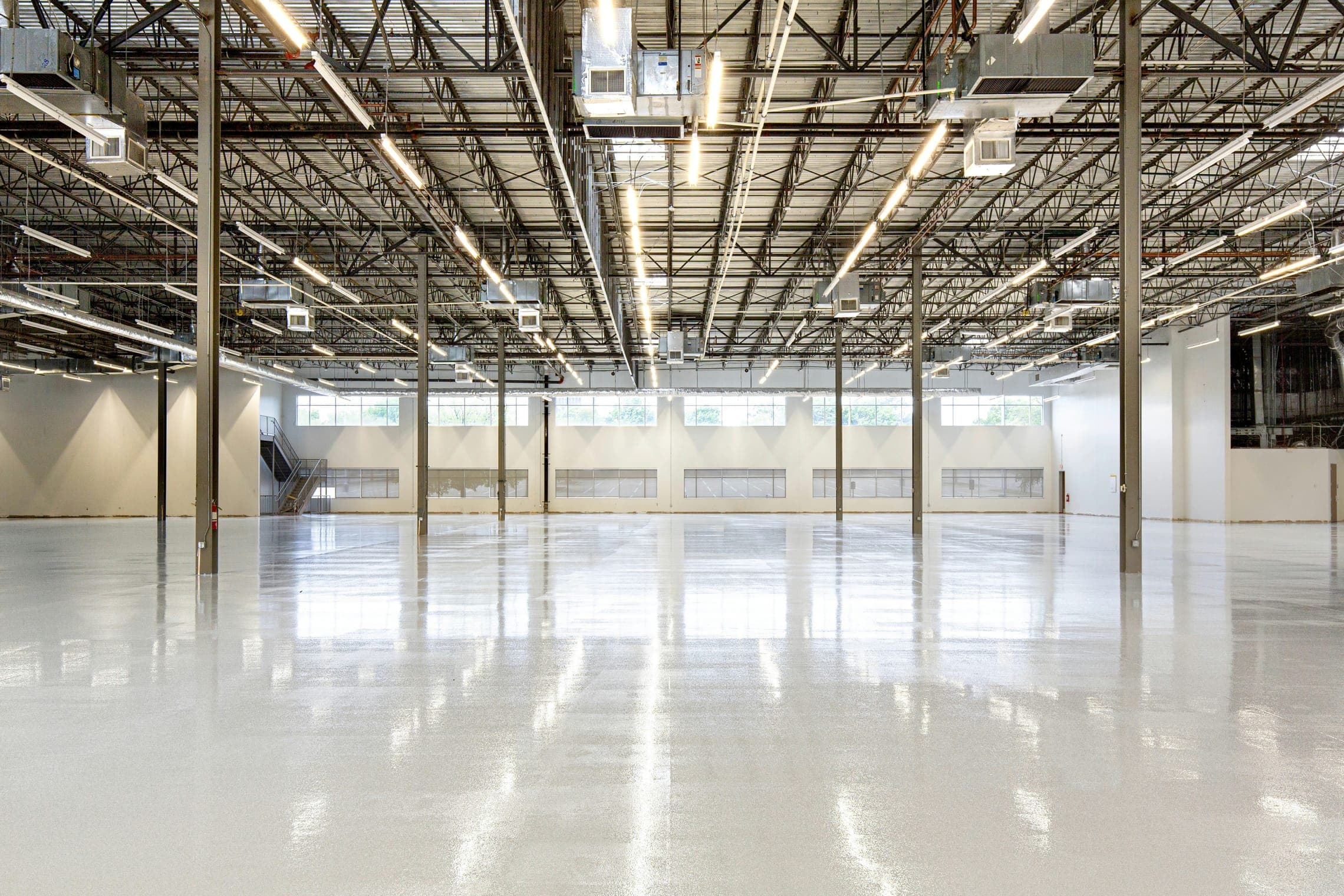Vast empty hall with exposed steel trusses, white epoxy floor and clerestory windows.