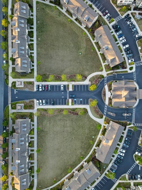 Aerial view of apartment buildings around lawns, parking lots and a roundabout.