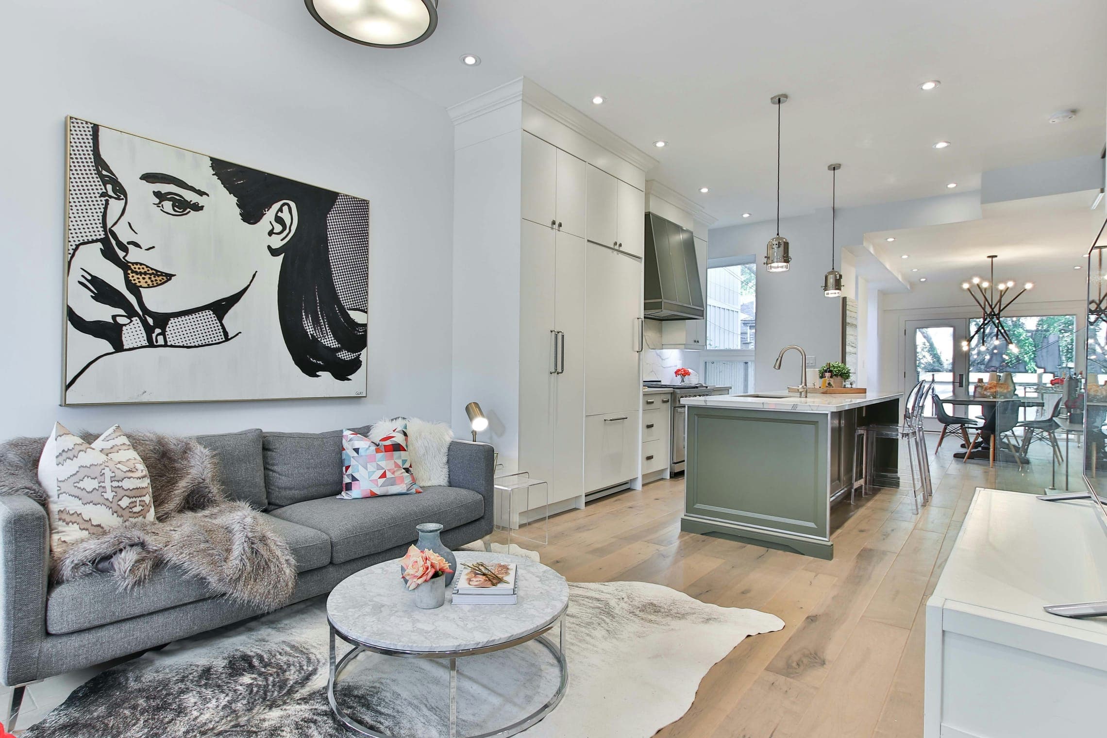 Open-plan living room and kitchen with grey sofa, large pop-art painting and island.