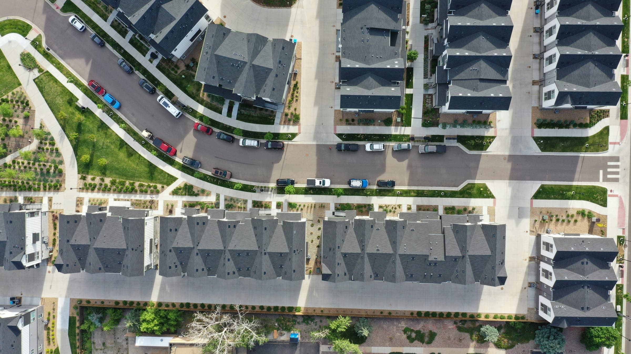 Aerial view of rows of grey-roofed townhouses along a street with parked cars.