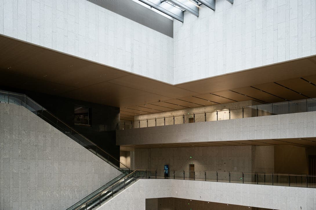 Atrium with pale stone walls, wooden ceilings, glass balustrades and a long escalator.