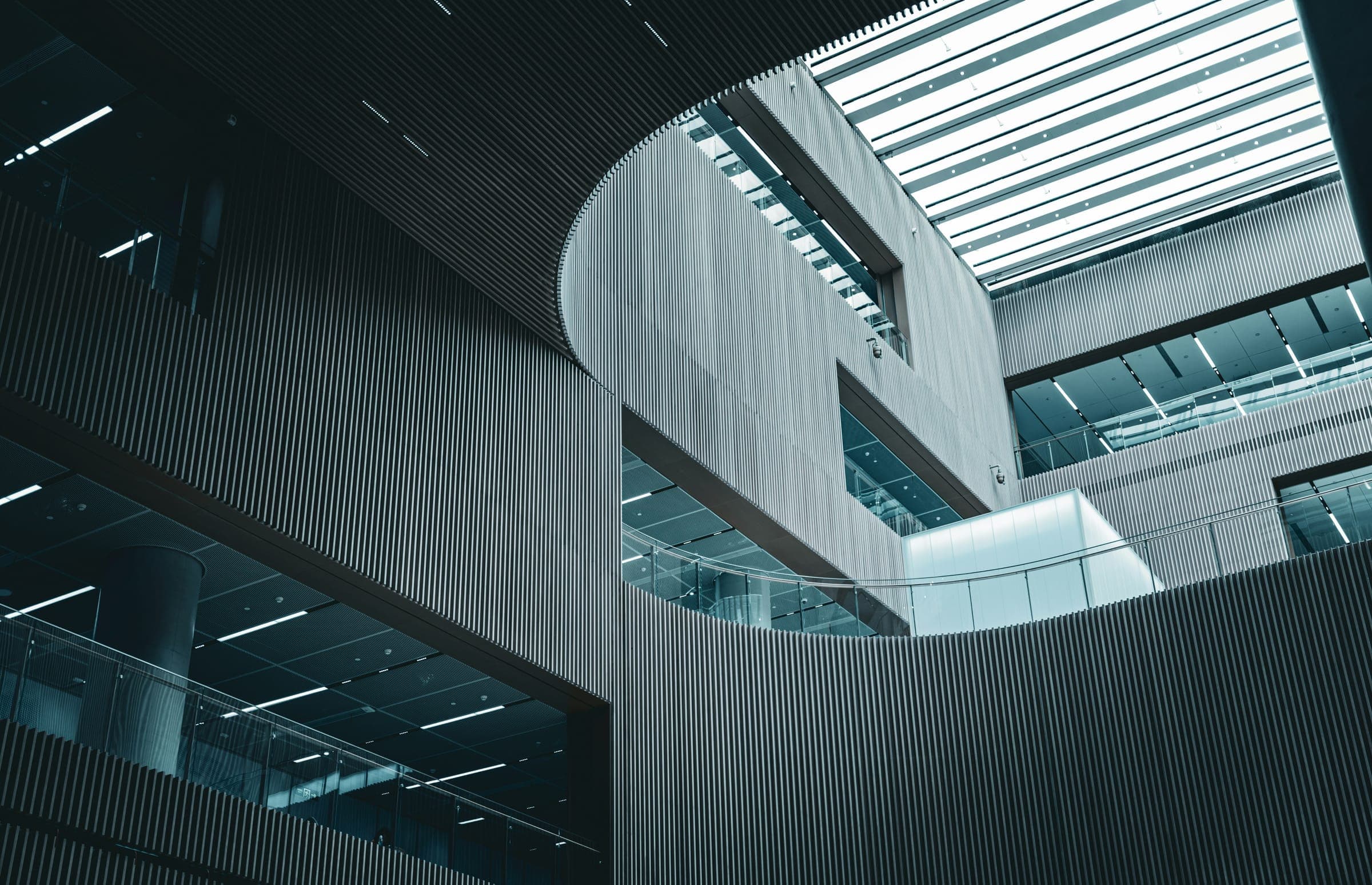 Atrium with grey slatted walls, curved openings, glass balconies and a long skylight.
