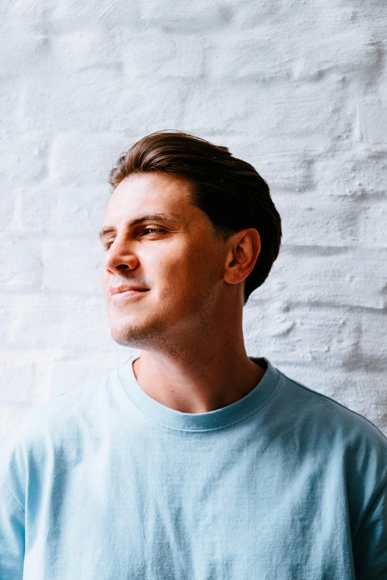 Portrait of Benjamin Harris, smiling man in a light blue T-shirt against a white brick wall.