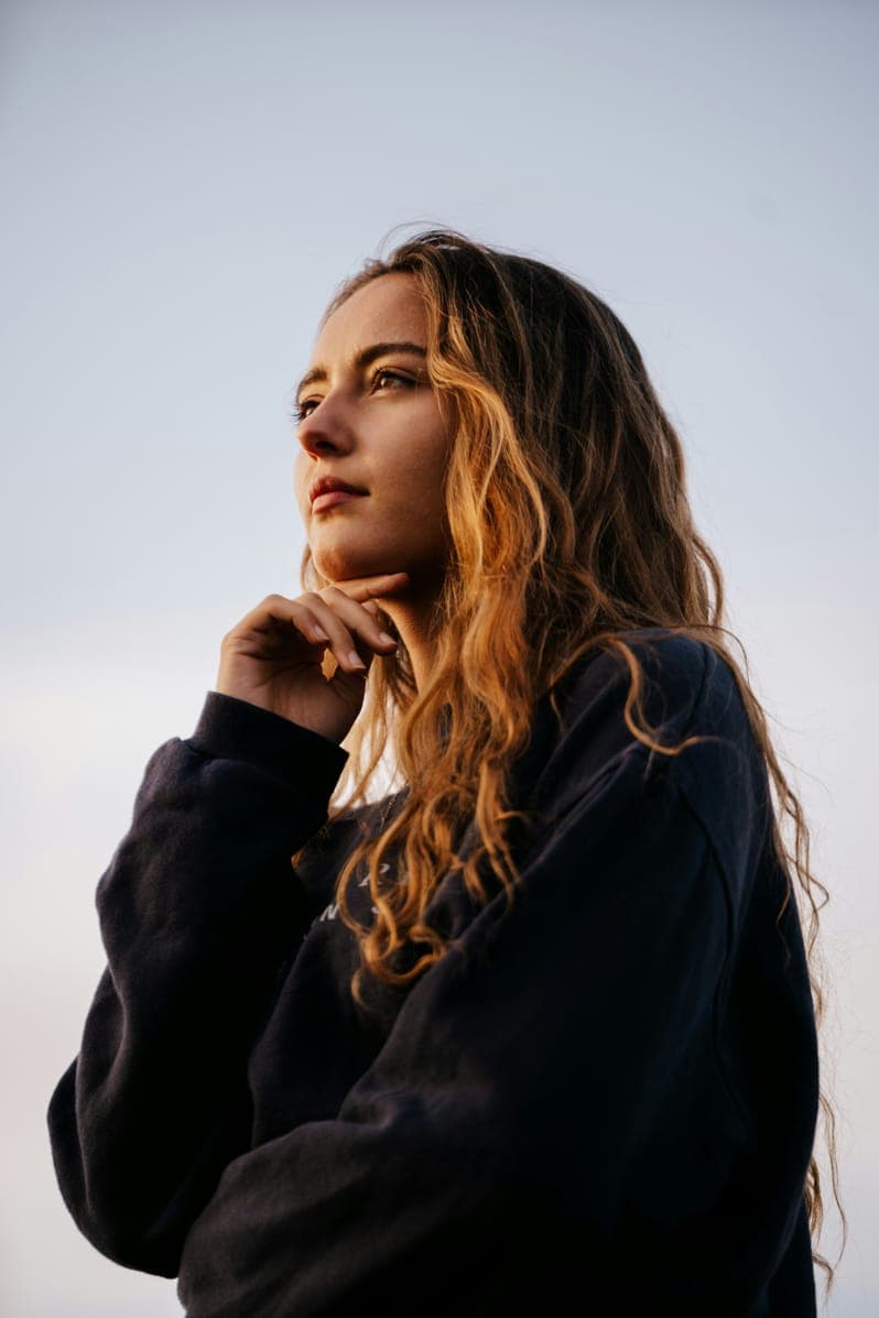 Portrait of Harper Collins, woman with long wavy hair in a dark sweatshirt at golden hour.
