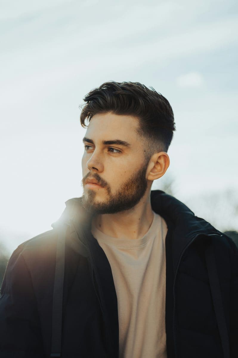 Portrait of James Wilson, bearded man in a black jacket against a bright hazy sky.