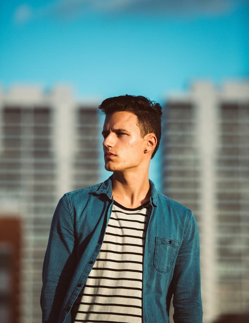 Portrait of Liam Anderson, young man in a denim shirt with blurred tall buildings behind.