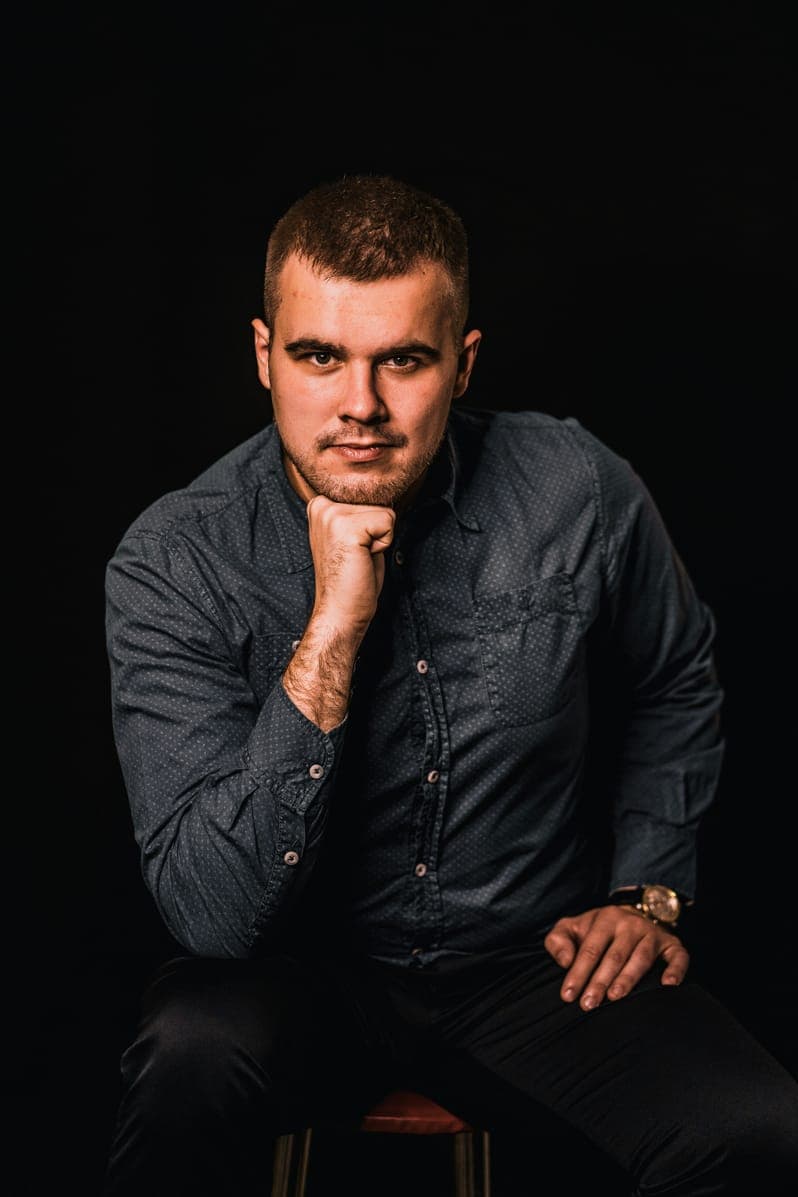 Portrait of Mason Walker, seated man in a dark shirt, chin on fist, black background.