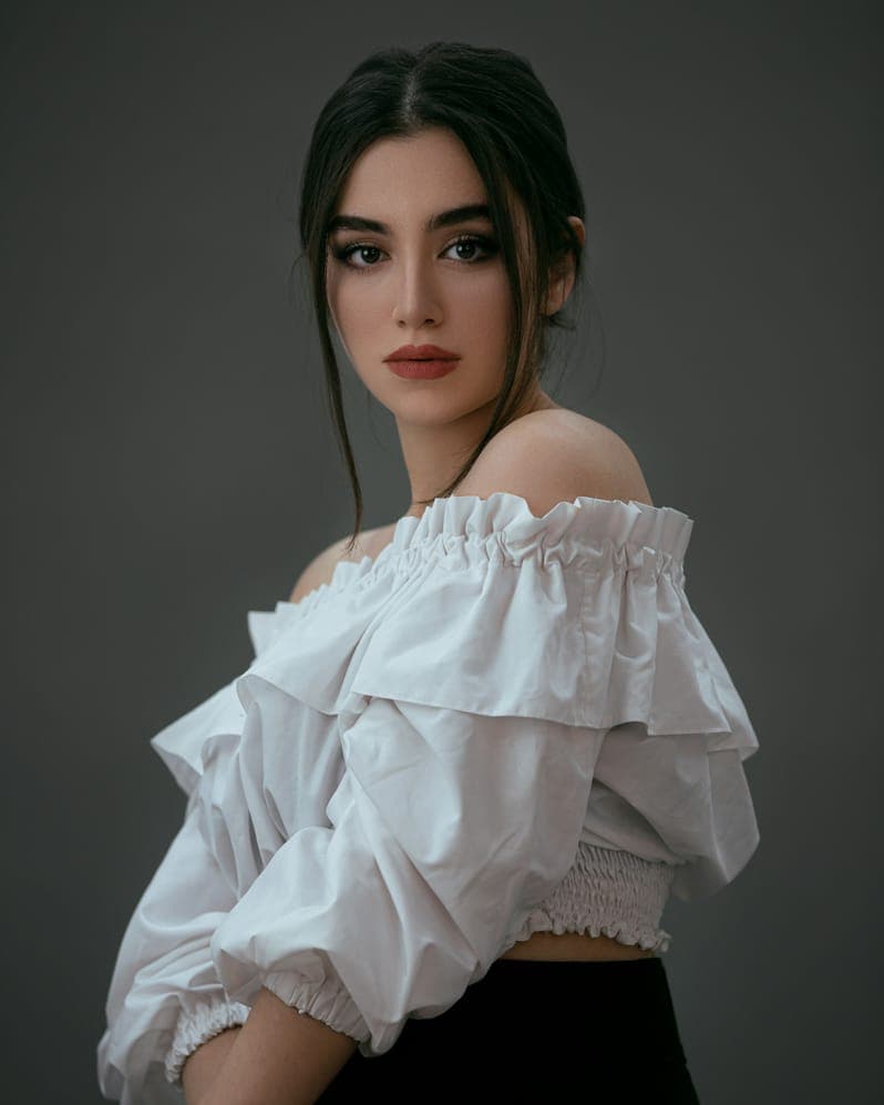 Portrait of Sophia Bennett, dark-haired woman in an off-shoulder white ruffled blouse, grey backdrop.
